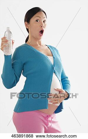Pregnant woman looking shocked and holding a water bottle View Large Photo Image Stock Photo - Pregnant woman looking shocked and holding a water bottle. Fotosearch