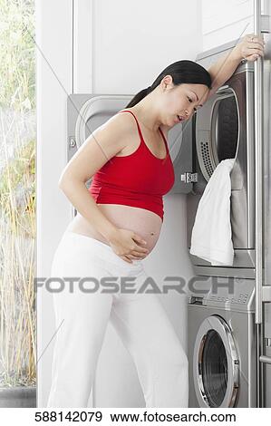 Pregnant woman looking tired in front of a washing machine View Large Photo Image Stock Photo - Pregnant woman looking tired in front of a washing machine. Fotosearch