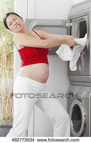 Pregnant woman pulling clothes from a washing machine View Large Photo Image Picture - Pregnant woman pulling clothes from a washing machine. Fotosearch