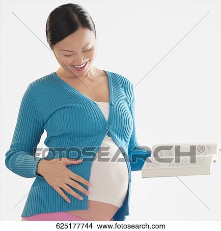 Pregnant woman touching her abdomen and holding a book View Large Photo Image Picture - Pregnant woman touching her abdomen and holding a book. Fotosearch