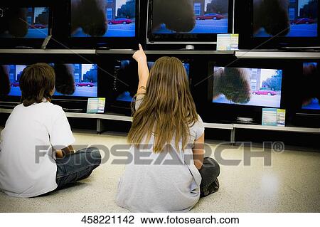 Rear view of a boy and a girl watching television in a supermarket View Large Photo Image Stock Image - Rear view of a boy and a girl watching television in a supermarket. Fotosearch