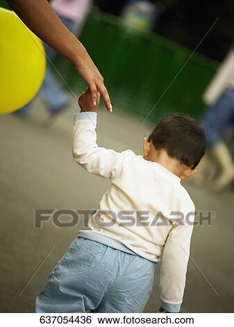 Rear view of a boy walking and holding a person's hand View Large Photo Image Stock Photograph - Rear view of a boy walking and holding a person's hand. Fotosearch