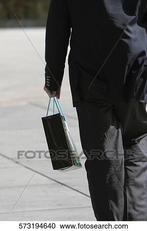 Stock Image - Rear view of a businessman carrying a shopping bag. Fotosearch
