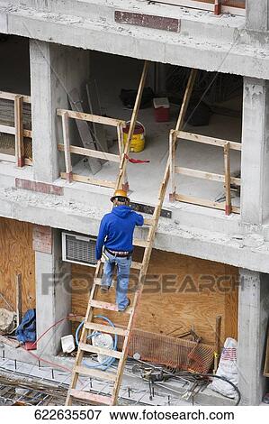 Stock Photo - Rear view of a construction worker moving up on a ladder at a construction site. Fotosearch