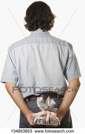 Rear view of a man hiding a gift behind him View Large Photo Image Stock Image - Rear view of a man hiding a gift behind him. Fotosearch