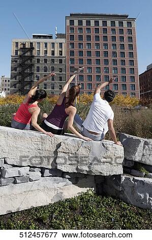 Stock Photo - Rear view of a man with two women exercising on a rock. Fotosearch
