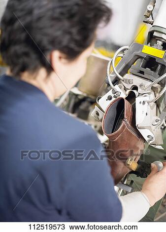 Stock Image - Rear view of a mid adult woman working in a shoe factory. Fotosearch