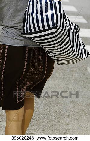 Rear view of a woman carrying a bag and walking on the road View Large Photo Image Stock Photograph - Rear view of a woman carrying a bag and walking on the road. Fotosearch