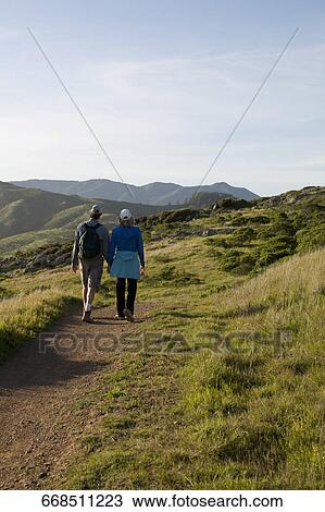 Rear view of two hikers walking on a footpath View Large Photo Image Stock Image - Rear view of two hikers walking on a footpath. Fotosearch