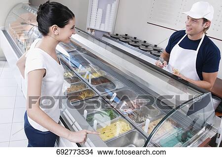 Picture - Sales clerk attending a customer in an ice cream parlor. Fotosearch