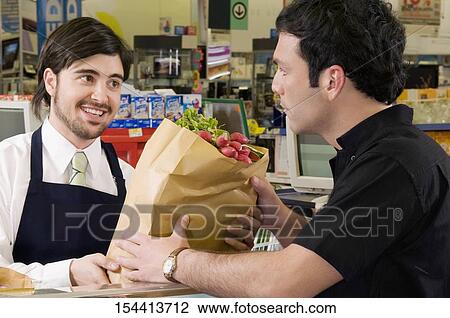 Stock Image - Sales clerk giving a grocery bag to a costumer in a supermarket. Fotosearch