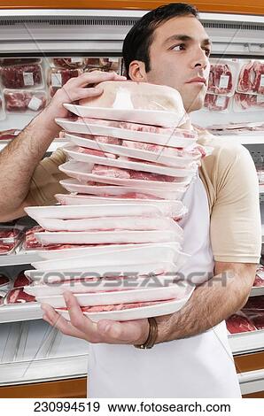 Stock Photo - Sales clerk holding a stack of meat in a supermarket. Fotosearch