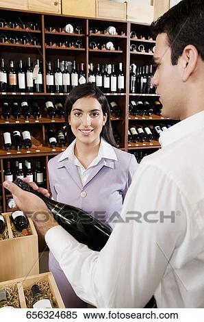 Sales clerk holding a wine bottle beside a businesswoman smiling View Large Photo Image Stock Photography - Sales clerk holding a wine bottle beside a businesswoman smiling. Fotosearch