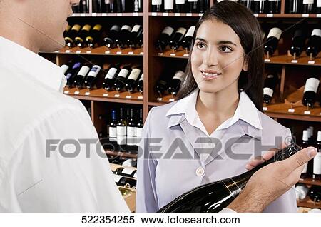 Sales clerk holding a wine bottle with a businesswoman smiling View Large Photo Image Stock Photography - Sales clerk holding a wine bottle with a businesswoman smiling. Fotosearch