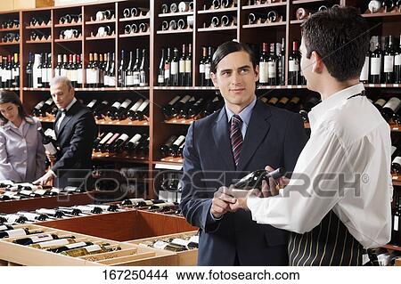Sales clerk showing a wine bottle to a customer View Large Photo Image Picture - Sales clerk showing a wine bottle to a customer. Fotosearch