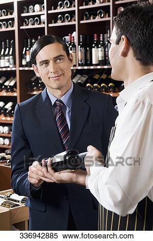 Sales clerk showing a wine bottle to a customer View Large Photo Image Stock Photography - Sales clerk showing a wine bottle to a customer. Fotosearch