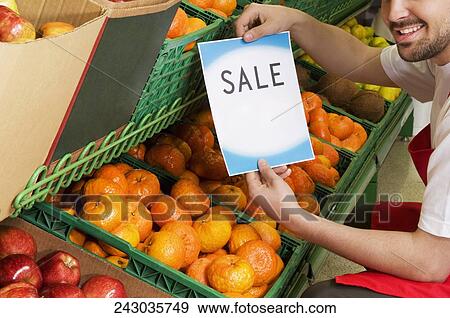 Salesman showing a Sale signboard over fruits' crates View Large Photo Image Stock Photo - Salesman showing a Sale signboard over fruits' crates. Fotosearch
