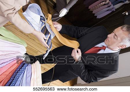 Stock Image - Saleswoman assisting a businessman in a clothing store. Fotosearch