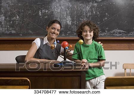 Stock Photo - Schoolboy and his teacher with model of solar system in a classroom. Fotosearch