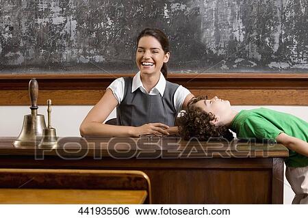 Schoolboy bending backward on a table with his teacher smiling View Large Photo Image Stock Photograph - Schoolboy bending backward on a table with his teacher smiling. Fotosearch