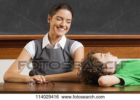Stock Photograph - Schoolboy lying on a table with his teacher smiling. Fotosearch