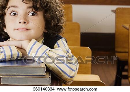 Picture - Schoolboy sitting with books in a classroom. Fotosearch