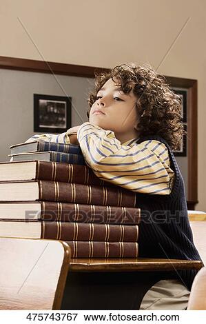 Stock Photo - Schoolboy sitting with books in a classroom. Fotosearch
