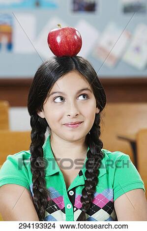 Picture - Schoolgirl carrying an apple on her head in a classroom. Fotosearch