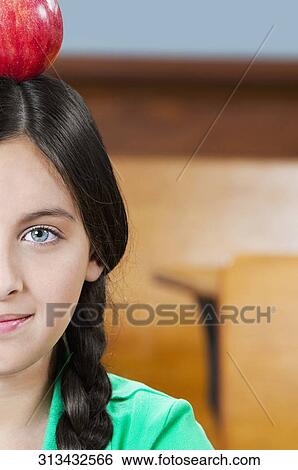 Schoolgirl carrying an apple on her head in a classroom View Large Photo Image Stock Photograph - Schoolgirl carrying an apple on her head in a classroom. Fotosearch