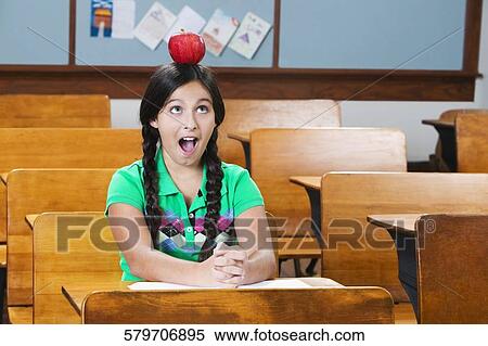 Schoolgirl carrying an apple on her head in a classroom View Large Photo Image Stock Photography - Schoolgirl carrying an apple on her head in a classroom. Fotosearch