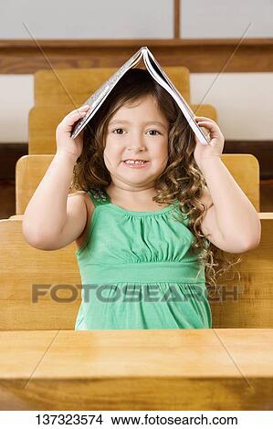Schoolgirl holding a book on her head in a classroom View Large Photo Image Picture - Schoolgirl holding a book on her head in a classroom. Fotosearch