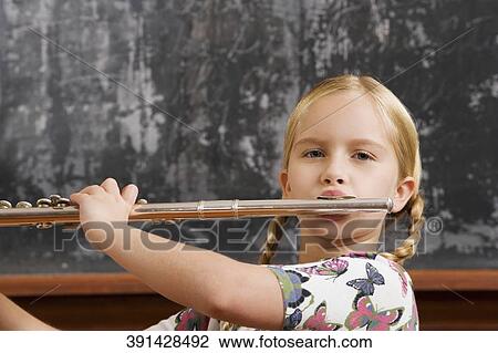 Stock Image - Schoolgirl playing a flute in a classroom. Fotosearch