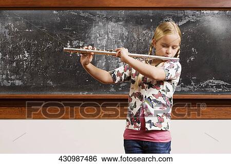 Stock Photograph - Schoolgirl playing a flute in a classroom. Fotosearch