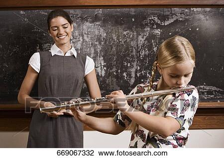 Schoolgirl playing a flute with her teacher smiling in front of a blackboard View Large Photo Image Stock Image - Schoolgirl playing a flute with her teacher smiling in front of a blackboard. Fotosearch