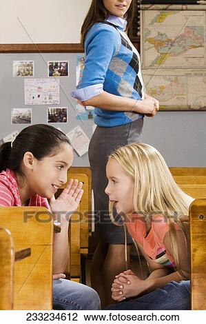 Schoolgirl whispering to her friend in a classroom View Large Photo Image Stock Image - Schoolgirl whispering to her friend in a classroom. Fotosearch