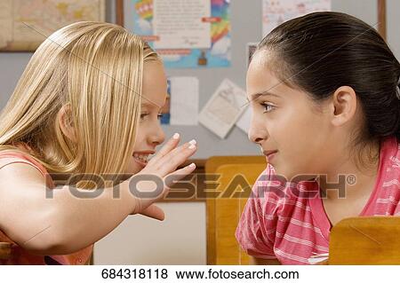 Schoolgirl whispering to her friend in a classroom View Large Photo Image Stock Photo - Schoolgirl whispering to her friend in a classroom. Fotosearch
