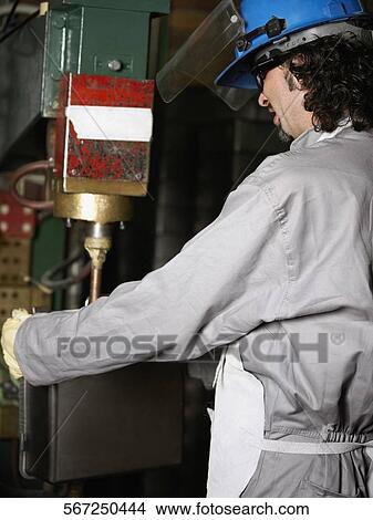 Picture - Side profile of a manual worker working on a spot welding machine. Fotosearch