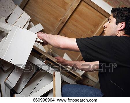 Picture - Side profile of a young man searching in a heap of scrap wood. Fotosearch
