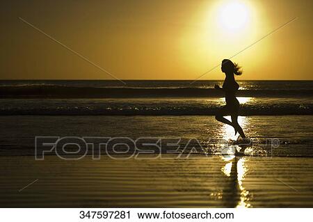 Stock Image - Silhouette of a woman running on the beach. Fotosearch