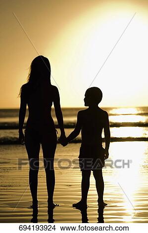 Silhouette of a woman with her son standing on the beach View Large Photo Image Picture - Silhouette of a woman with her son standing on the beach. Fotosearch