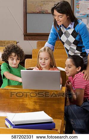 Students with their teacher using a laptop in a classroom View Large Photo Image Stock Image - Students with their teacher using a laptop in a classroom. Fotosearch