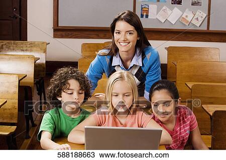Stock Image - Students with their teacher using a laptop in a classroom. Fotosearch