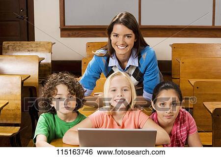 Students with their teacher using a laptop in a classroom View Large Photo Image Stock Photograph - Students with their teacher using a laptop in a classroom. Fotosearch