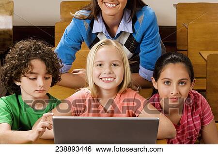 Stock Photograph - Students with their teacher using a laptop in a classroom. Fotosearch