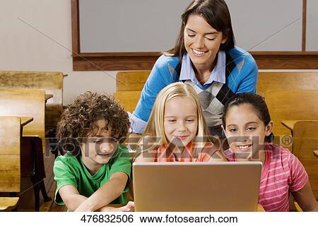 Stock Photograph - Students with their teacher using a laptop in a classroom. Fotosearch