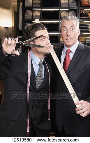 Tailor holding a scissors with a businessman in a clothing store View Large Photo Image Stock Image - Tailor holding a scissors with a businessman in a clothing store. Fotosearch
