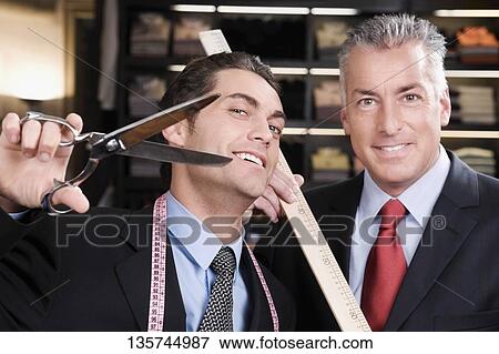 Stock Photo - Tailor holding a scissors with a businessman in a clothing store. Fotosearch