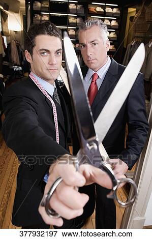 Tailor holding a scissors with a businessman in a clothing store View Large Photo Image Stock Photo - Tailor holding a scissors with a businessman in a clothing store. Fotosearch