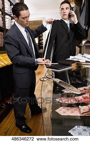 Stock Image - Tailor taking the measurements of a customer. Fotosearch