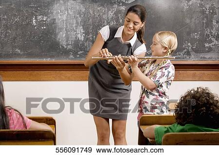 Teacher helping a schoolgirl playing a flute in a classroom View Large Photo Image Stock Photo - Teacher helping a schoolgirl playing a flute in a classroom. Fotosearch